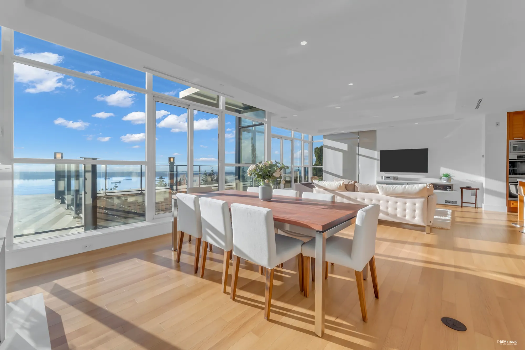Along the dining table toward the living room, the corner of windows and the terrace beyond