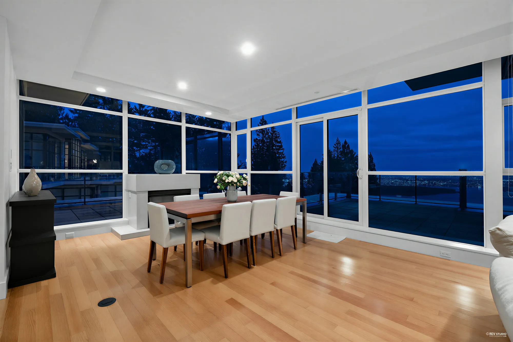 The dining area from the same place at dusk, the fireplace and the windows behind the table