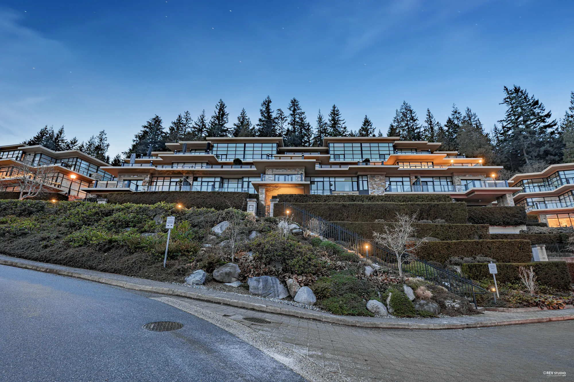 The terraced buildings from the drive at dusk, the windows and the garden lights on