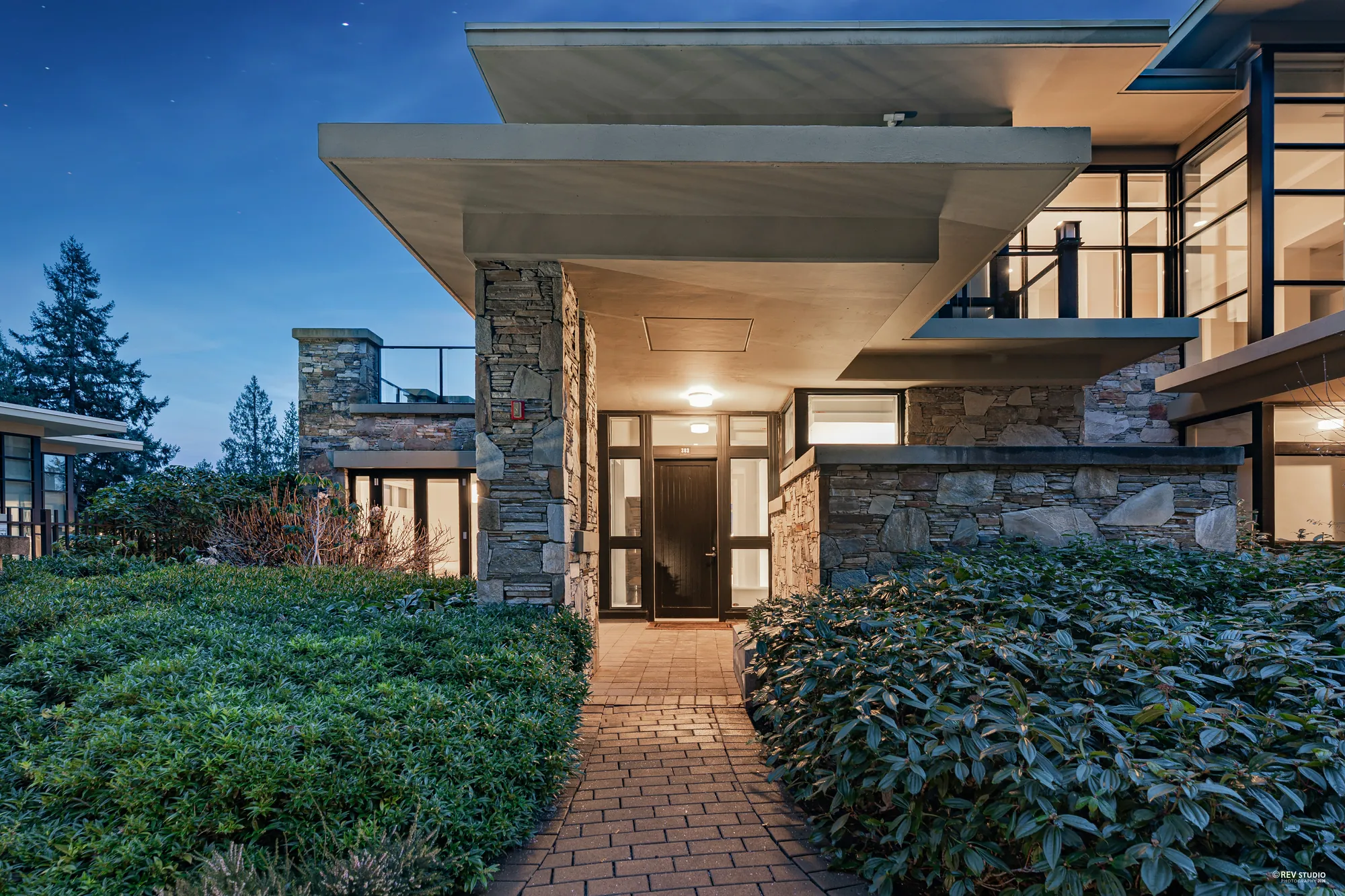 The same path and door at dusk, the light on under the overhang