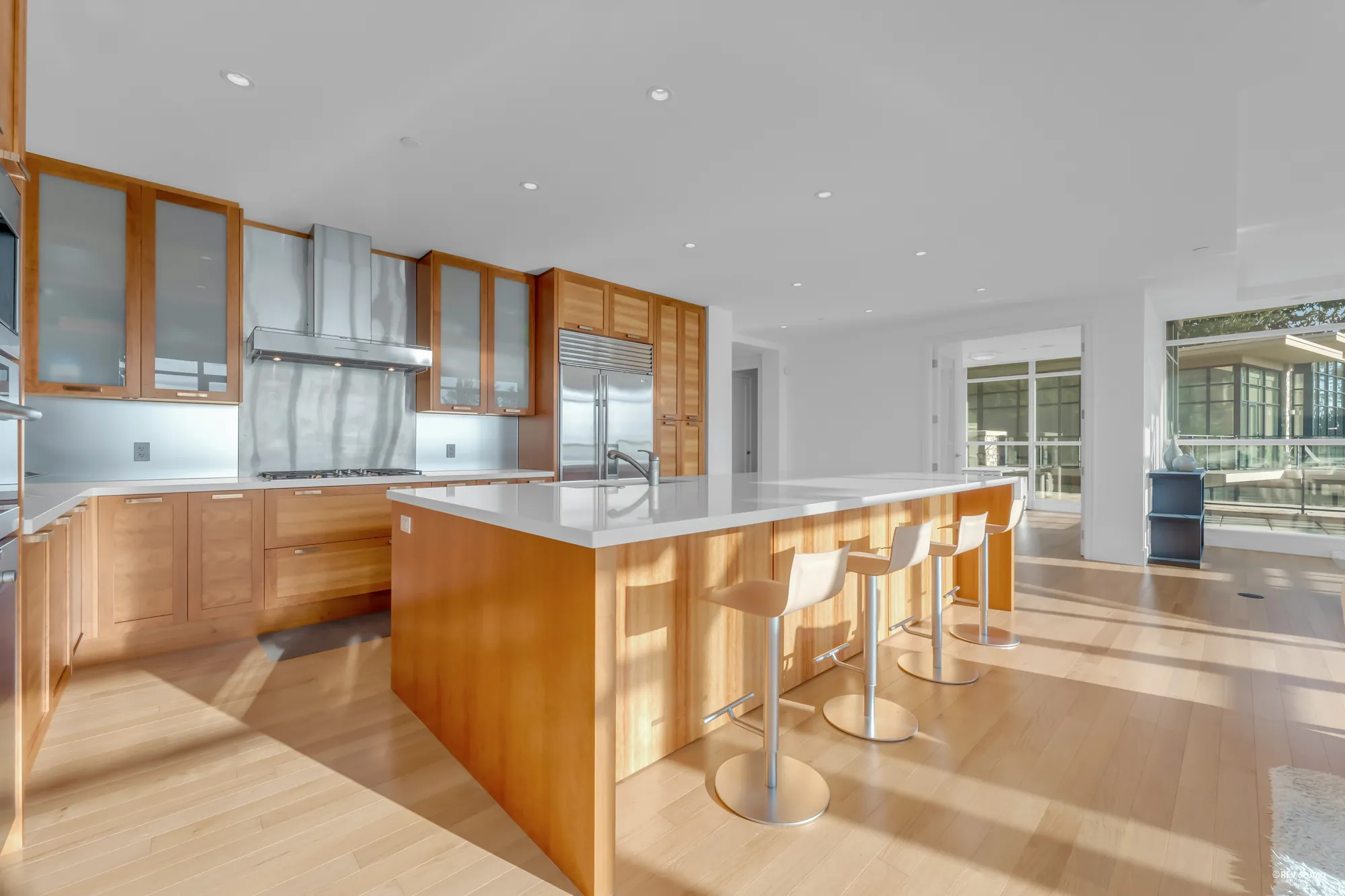 The kitchen: wood cabinetry to the ceiling, a stainless hood over the cooktop, glass-fronted upper cabinets, and a long island with a white counter and white stools