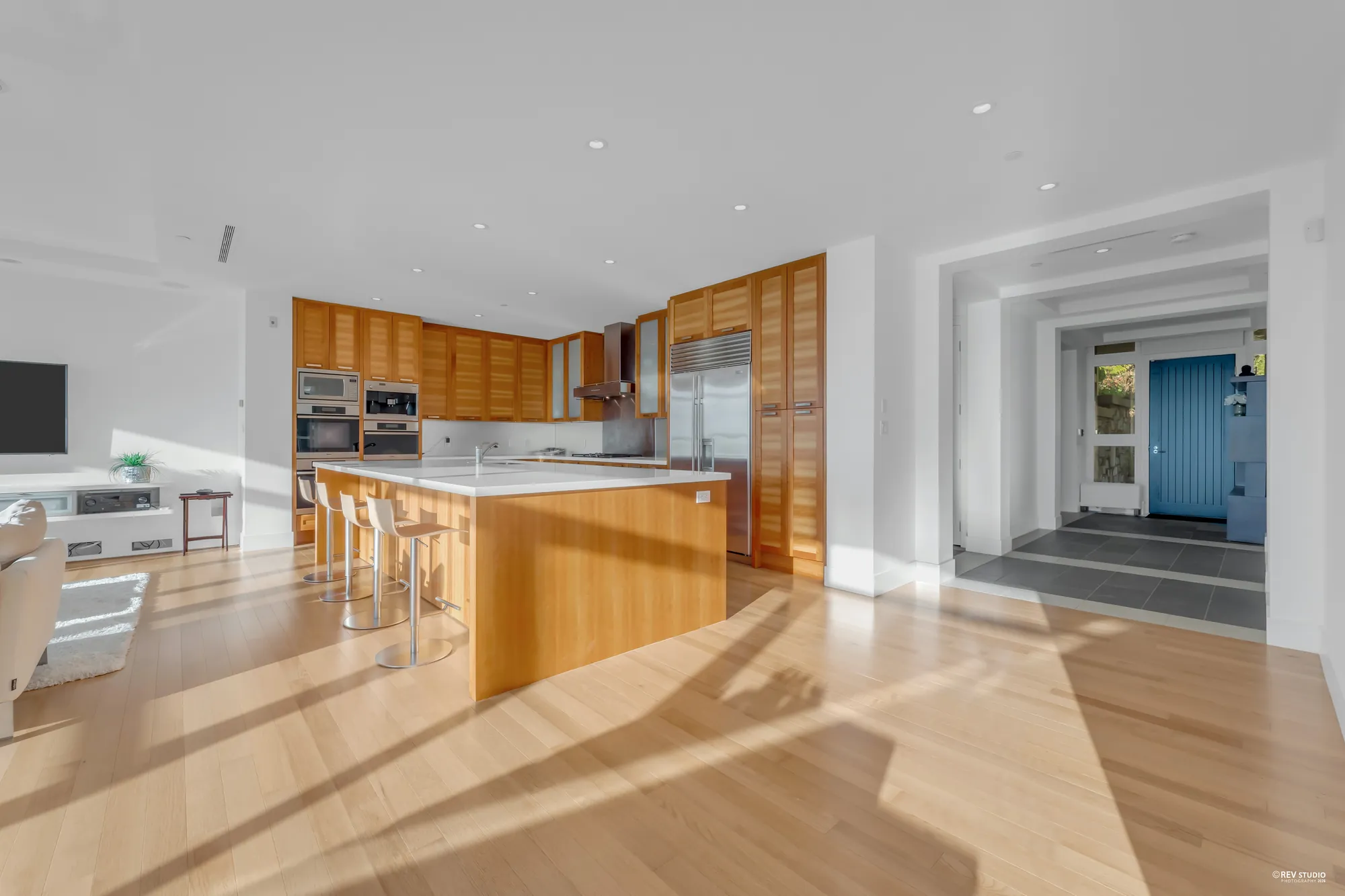 The kitchen from the living room, the island in front and, at the right, the hall to the foyer and the front door