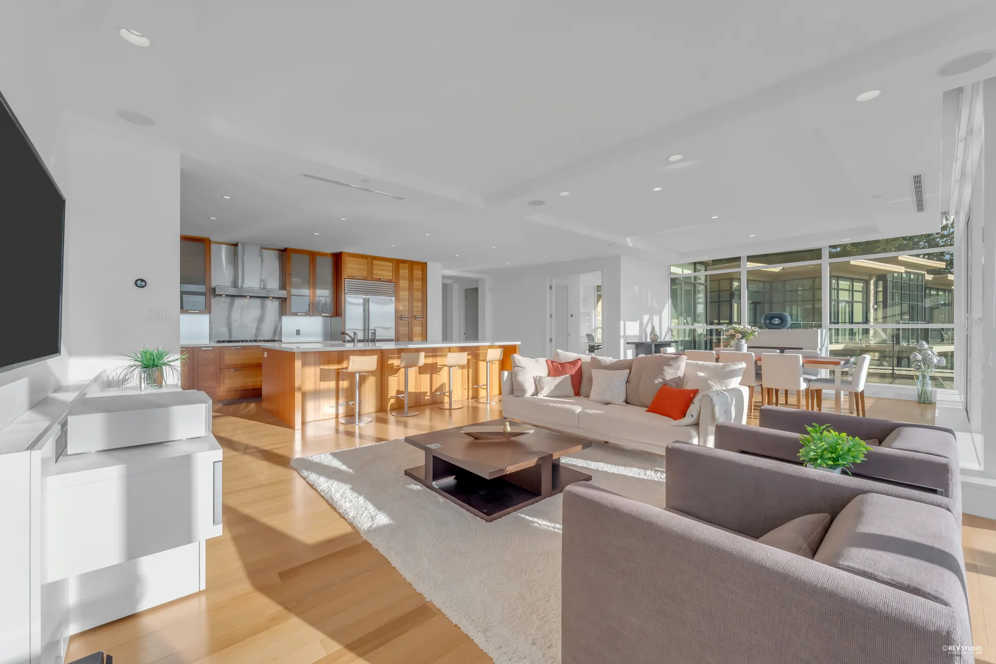 From the living room toward the kitchen: grey armchairs and the cream sofa in front, the wood-panelled kitchen and its island beyond