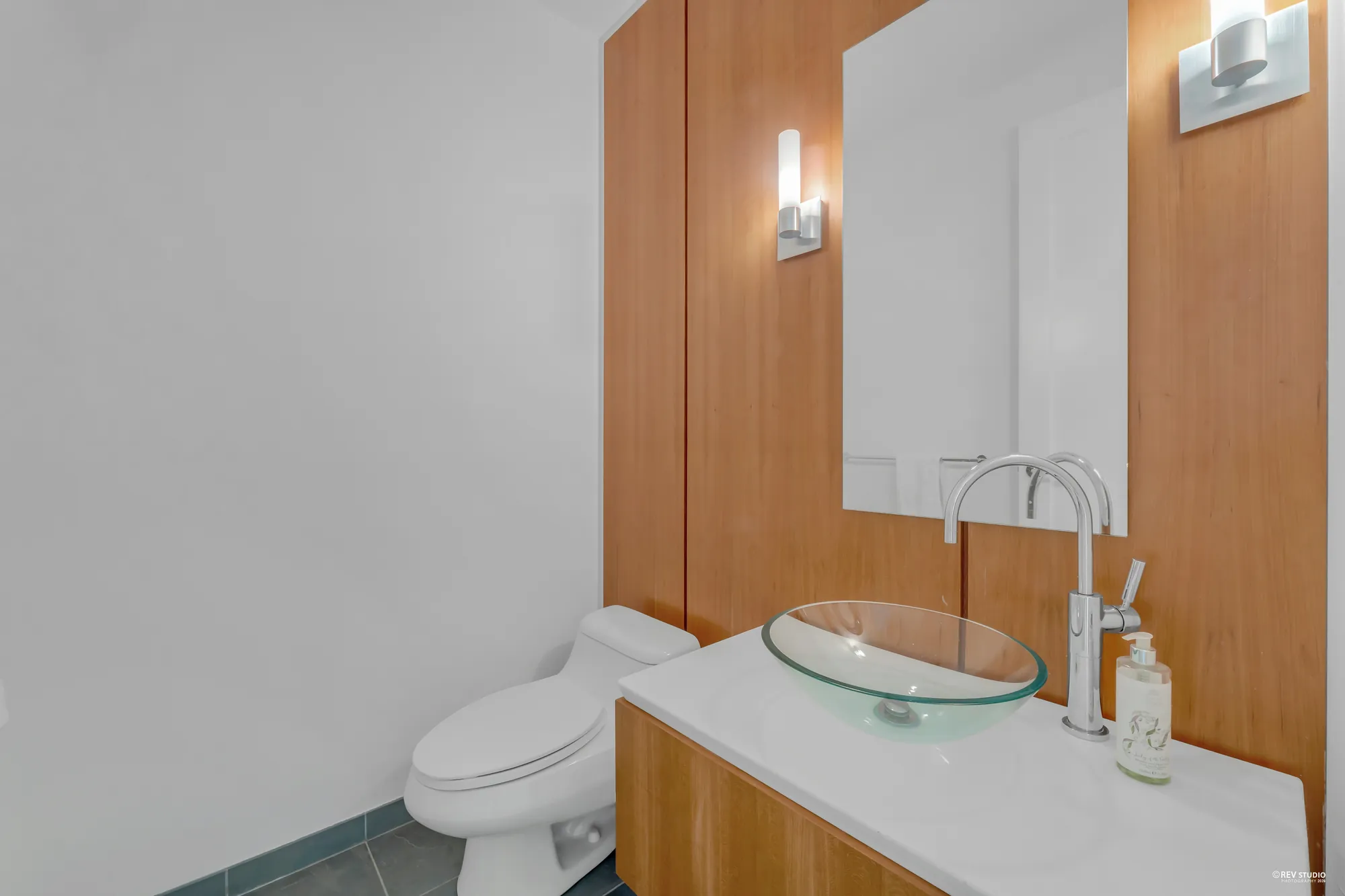 The powder room: a glass bowl sink on a white counter over a wood cabinet, a tall tap, a wood-panelled wall