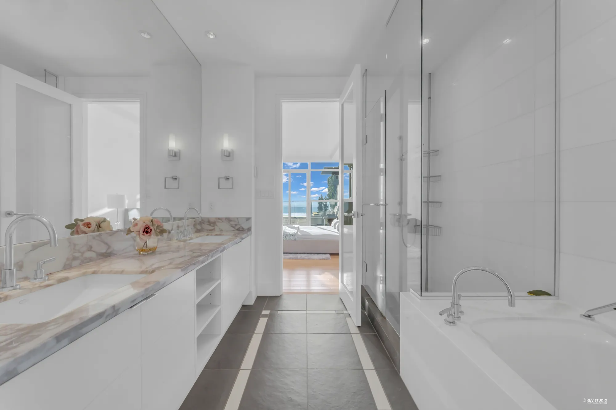 The primary bathroom from the other end: the stone counter, a soaking tub, the glass shower and the doorway to the bedroom
