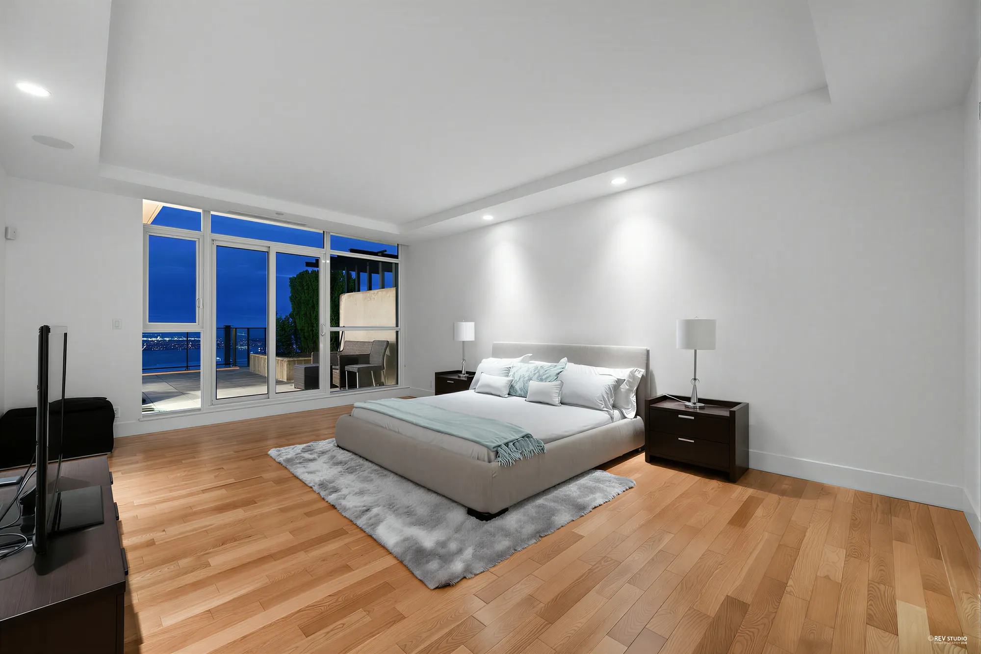 The same view of the primary bedroom at dusk, the windows deep blue
