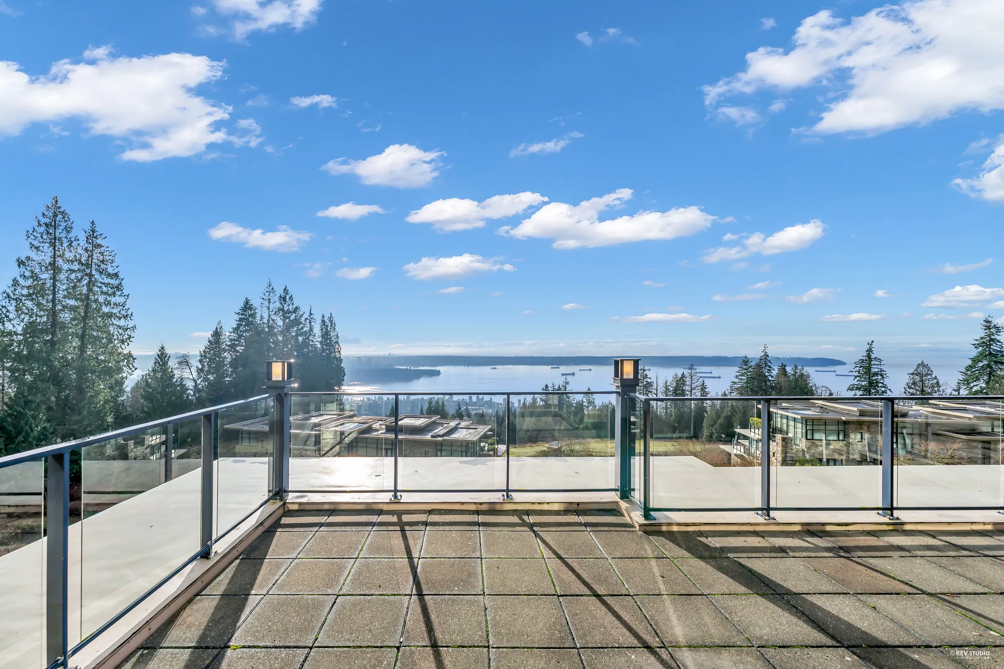 The terrace toward the water, the glass railing and its lamp posts, treetops below