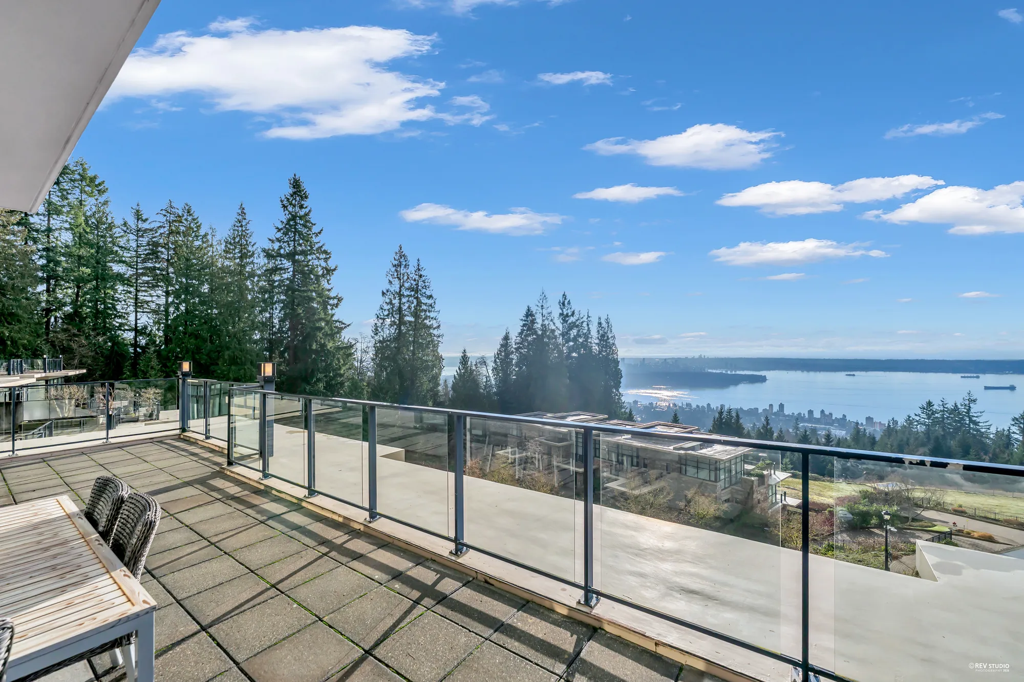 The terrace with a wood table and chairs at its edge, the glass railing and the water beyond